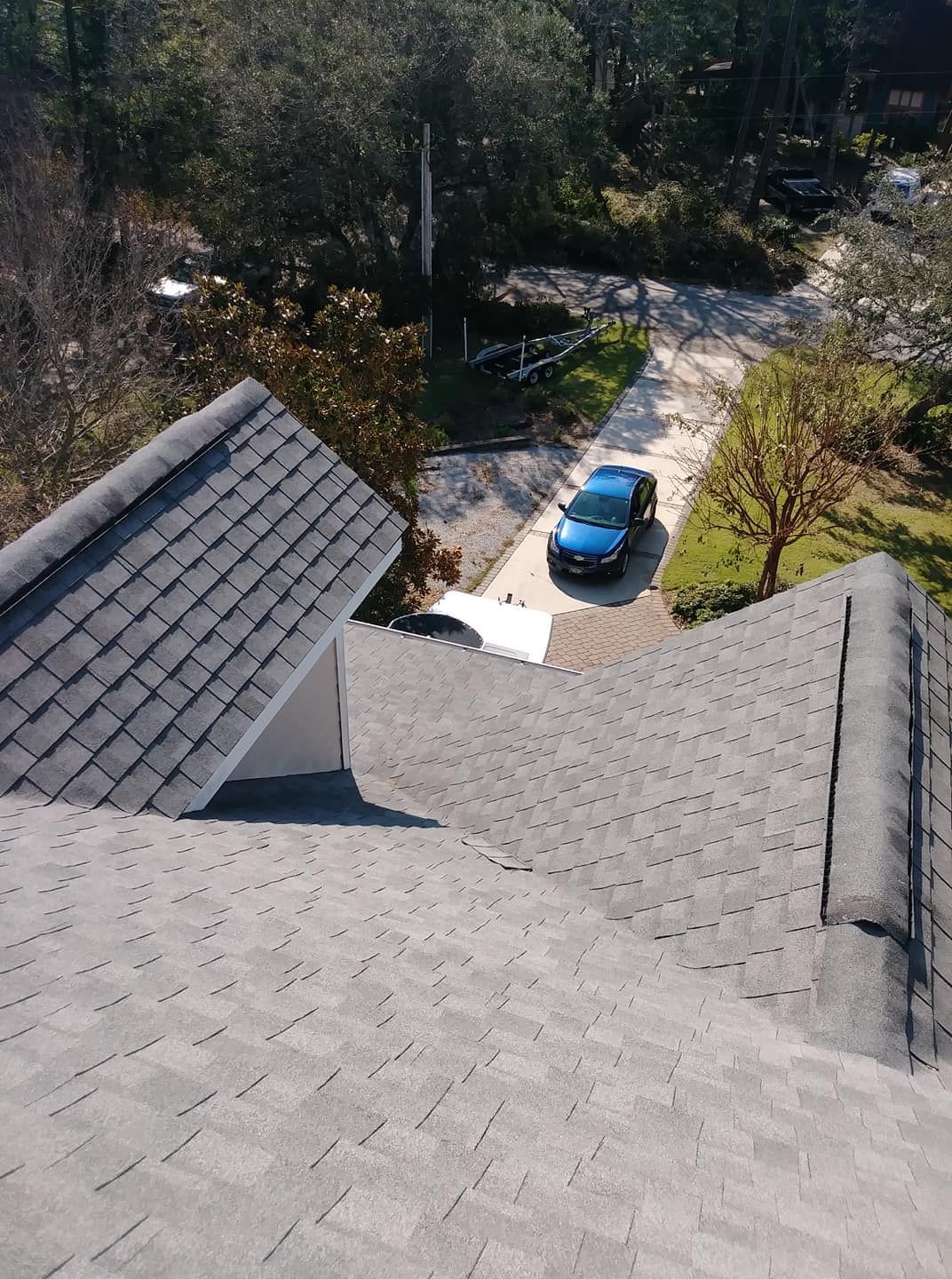 View from a rooftop of a blue car parked in a driveway near a house with gray shingles.