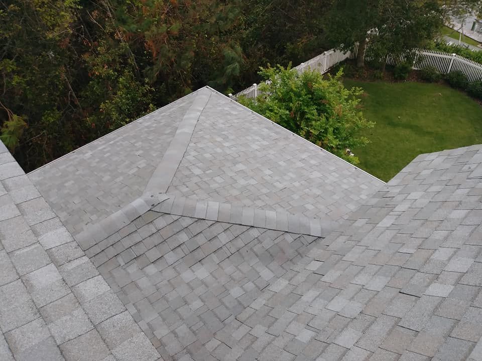 Gray shingle roof with a point, trees, and a white fence visible in the background.