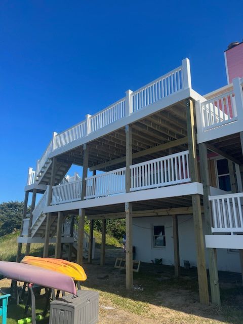 Construction workers building a small house with a porch and stairs outdoors on a sunny day.