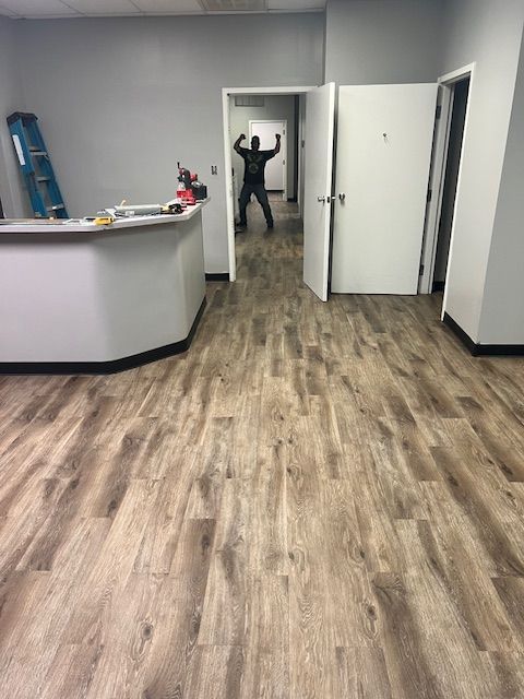 Interior office space with light wood-look floors, a reception desk, and a person in doorway with arms raised.