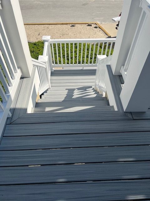 Staircase leading down, painted white with gray treads. Railings and sunlight present.