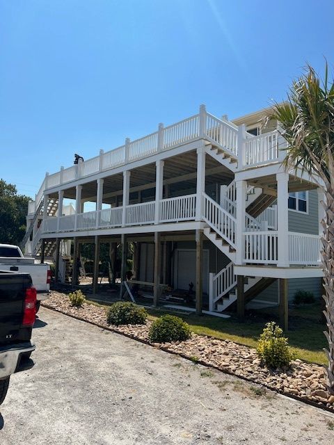 Two-story beach house with white railings, light green siding, and outdoor stairs.