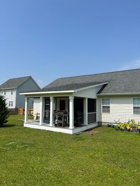 Screened porch addition on a white house, with columns, grill, and view of yard and sky.
