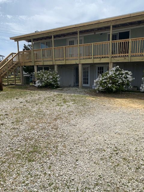 Two-story beach house with wooden deck, stairs, and gravel yard; hydrangeas in front.
