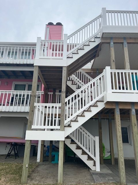 White wooden stairs leading up a pink house, with white railings. Cloudy sky.
