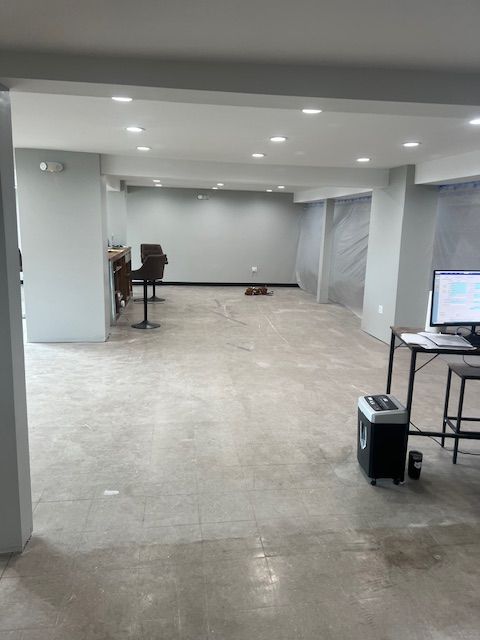 Empty, light-filled room with concrete floor, recessed lighting, and gray walls. Some furniture visible.