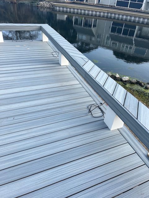 Dock with gray composite decking and a silver railing along a waterway, with houses reflected in the water.