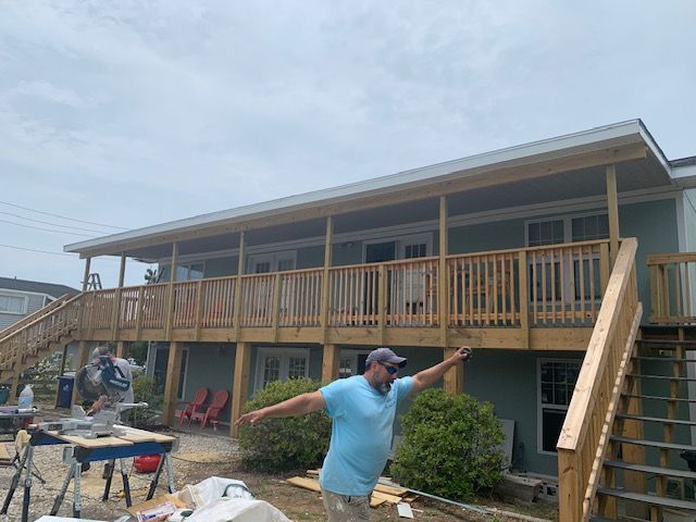 Construction worker with arms outstretched in front of a house with a newly built wooden deck.
