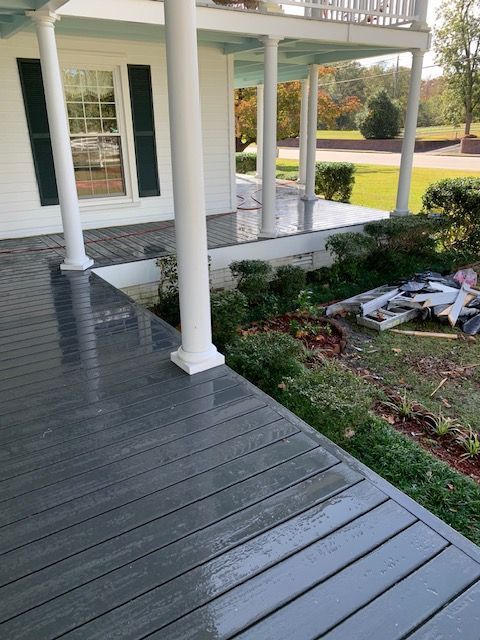 Gray painted porch with white columns, bushes, and part of a house.