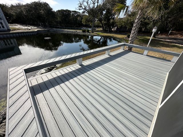 Gray composite deck overlooking a dark pond. Trees and a house are in the background.