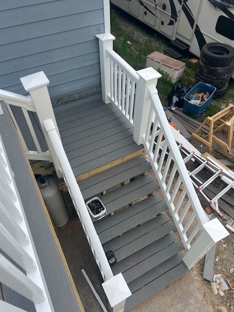 Gray wooden stairs with white railing, leading to a light blue house.