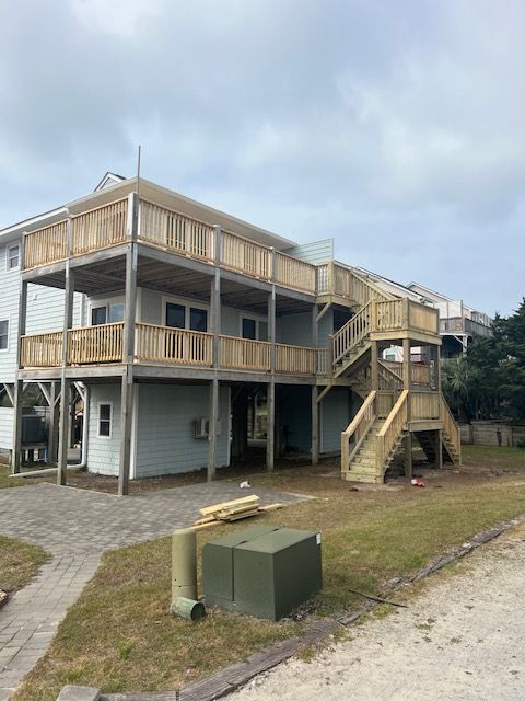Two-story light blue house with wooden decks and outdoor staircase; cloudy sky.