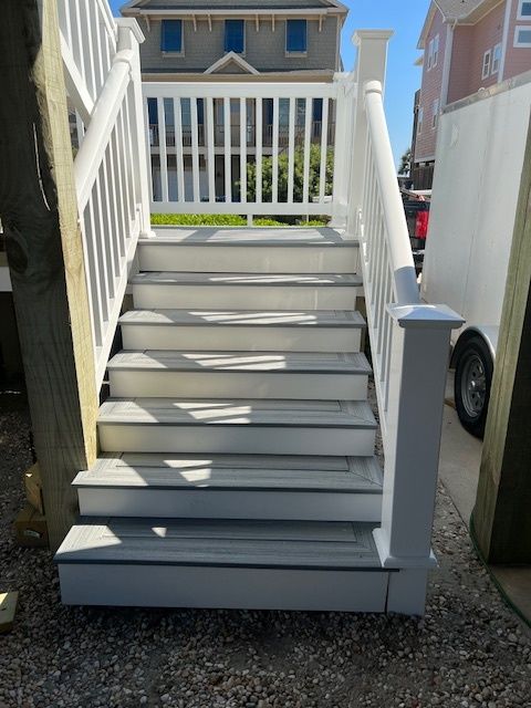 White staircase with gray steps leading up to a white railing; exterior setting.