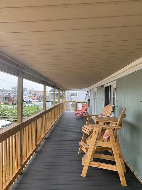 Covered wooden deck with seating, railing, and view of neighborhood.