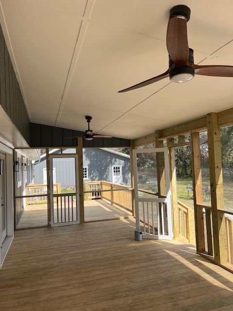 Screened porch with wood deck, two ceiling fans, and wooden railings. Overlooking a yard and buildings.