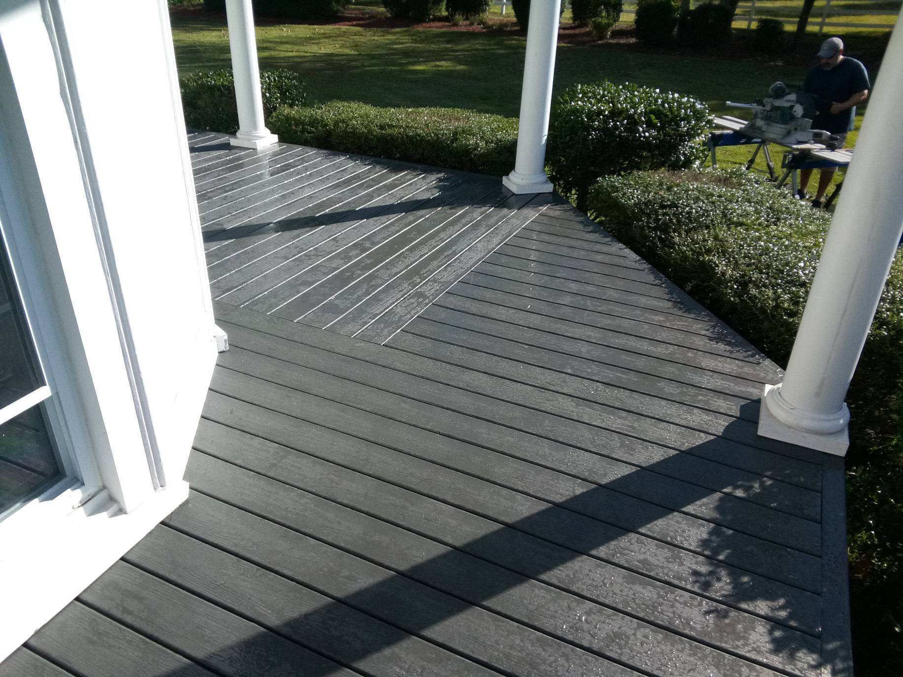 Gray composite deck with white columns and bushes. Man working in the background.