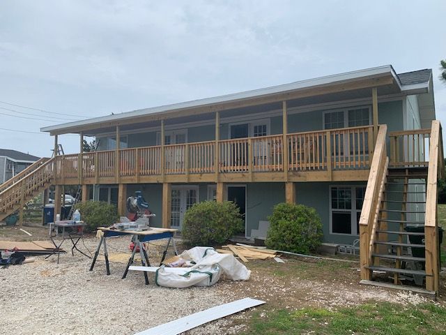 Two-story house with a wooden deck under construction; saw table and materials present.