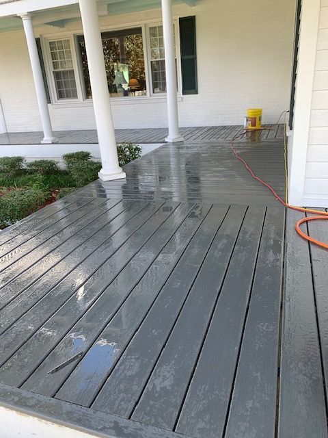 Wet, gray painted porch with white columns and house. A power washer hose is visible.