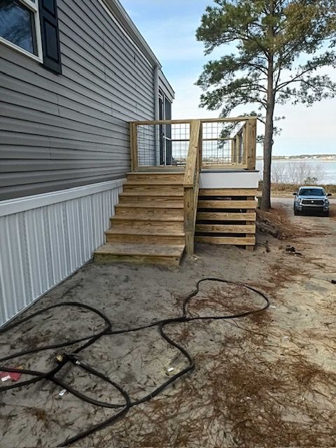Wooden steps and landing lead up to a mobile home's side entrance; a car is parked nearby.