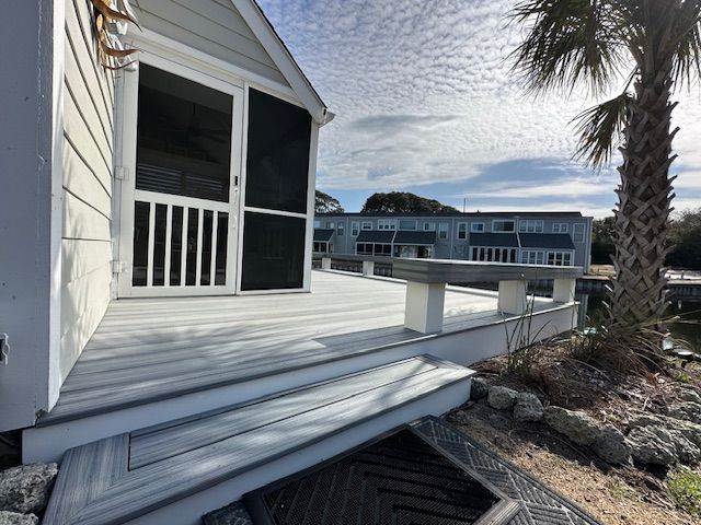 Grey deck with screened door, waterfront view, sunny day.