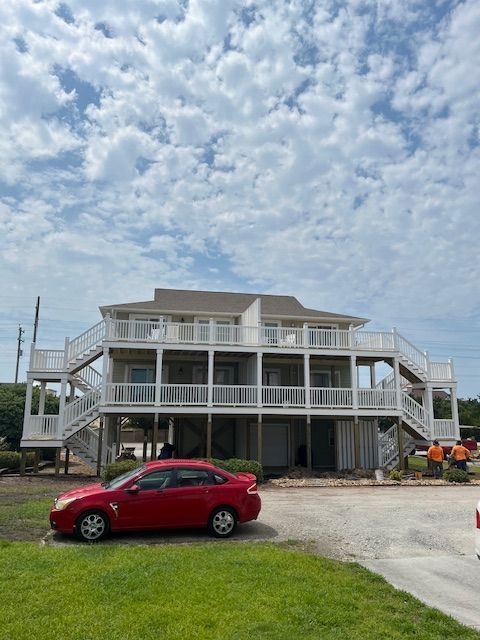 A red car parked in front of a two-story white building with decks and stairs; cloudy sky.
