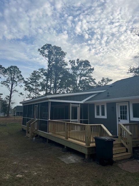 A house with a newly built wooden deck and screened porch, set against a cloudy sky.