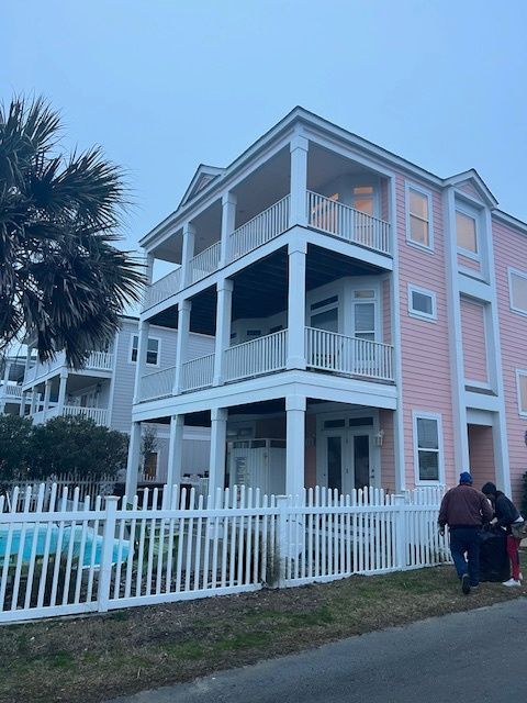 Pink multi-story house with white balconies and a picket fence; people by the entrance.