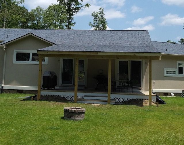 Backyard view of a beige house with a covered porch, green lawn, and a fire pit.