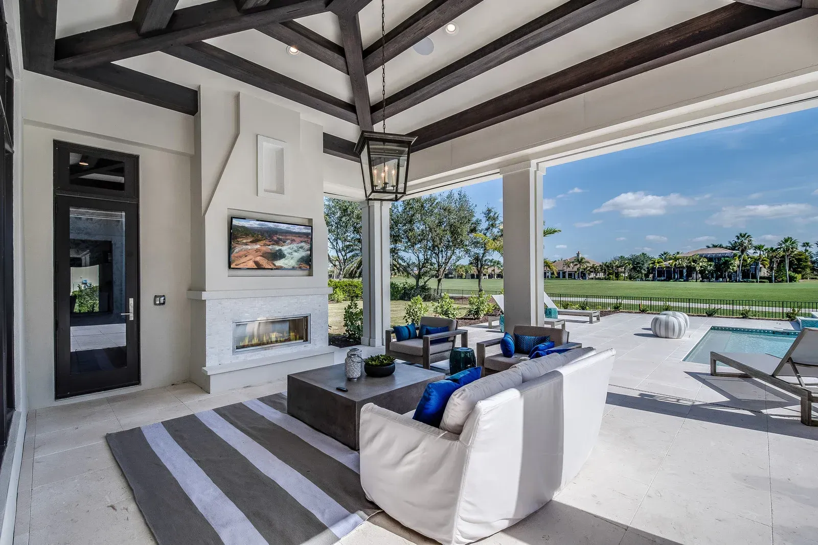 Covered outdoor patio with fireplace, TV, seating, and golf course view.