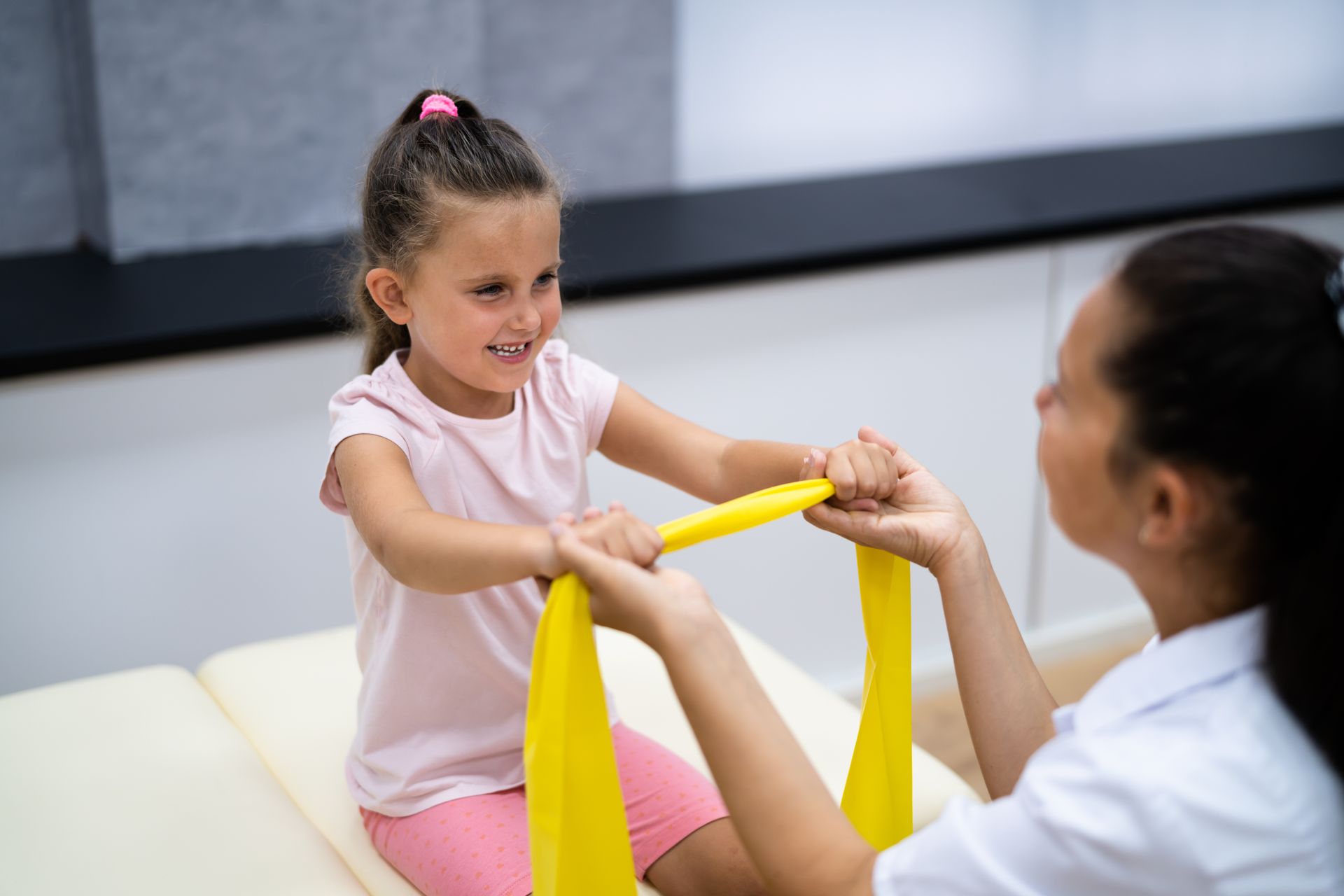Woman doing physical therapy with a child using a yellow resistance band