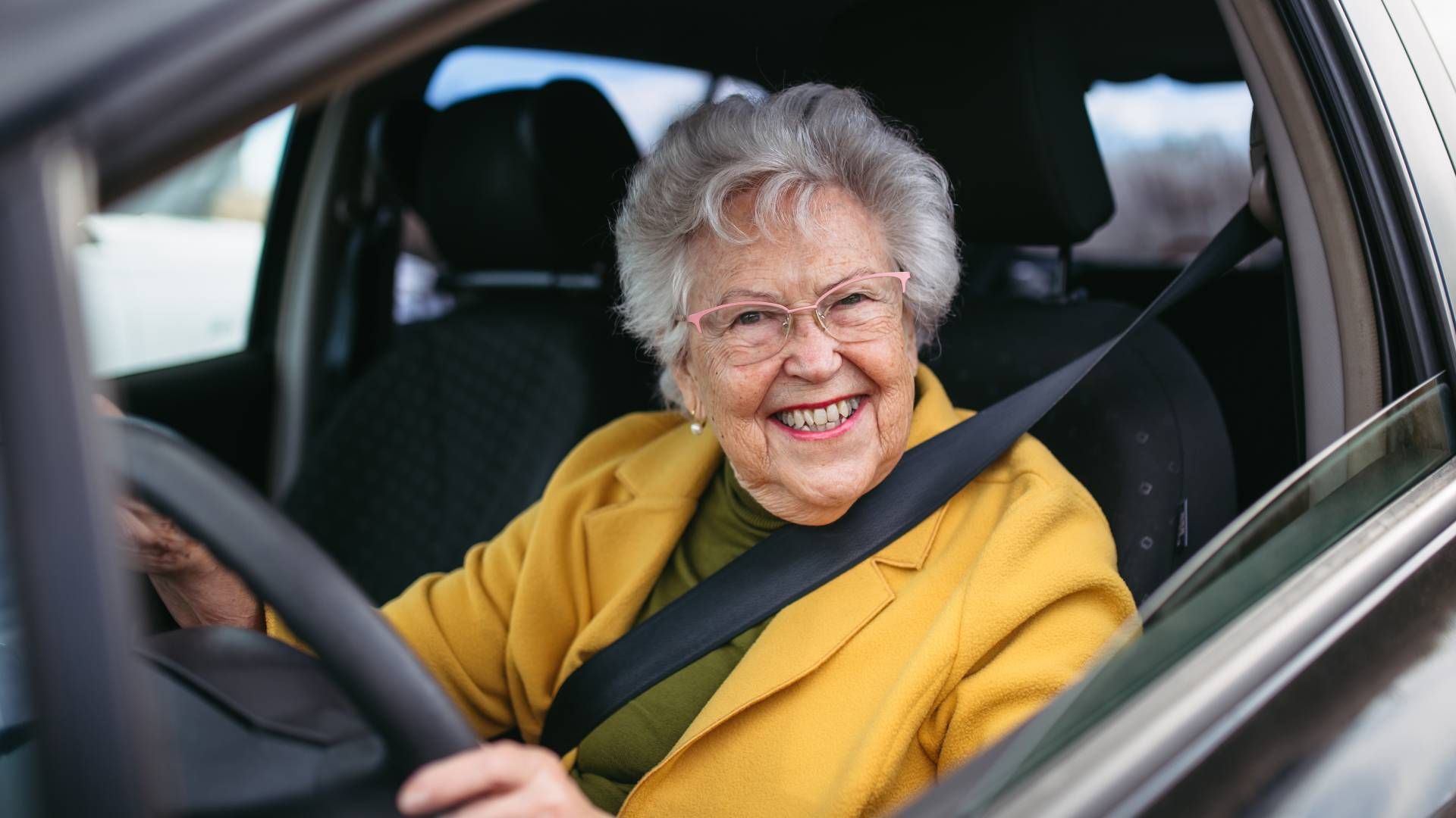 A Senior Lady sitting behind the wheel of a car, smiling widely at Family Choice Home Care near Lexi