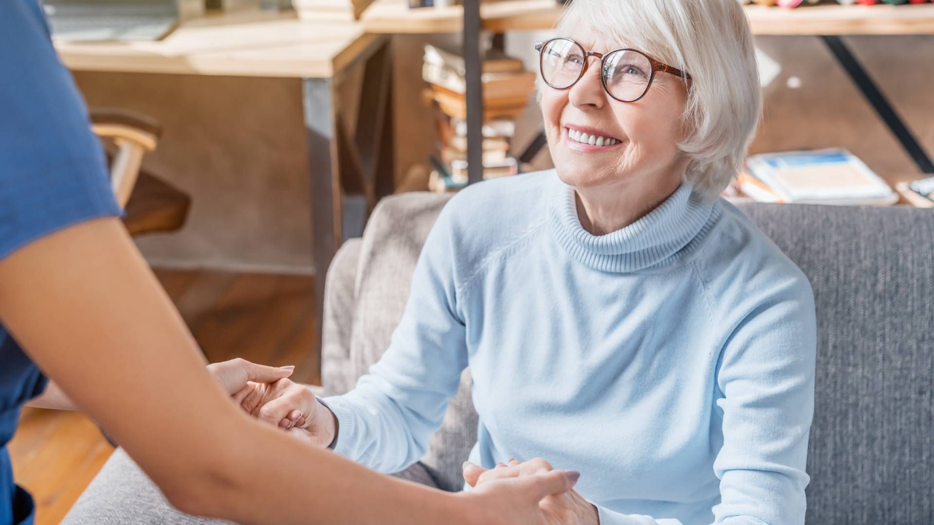 Nurse helping a smiling elderly woman stand up from a seat at Family Choice Home Care near Lexington