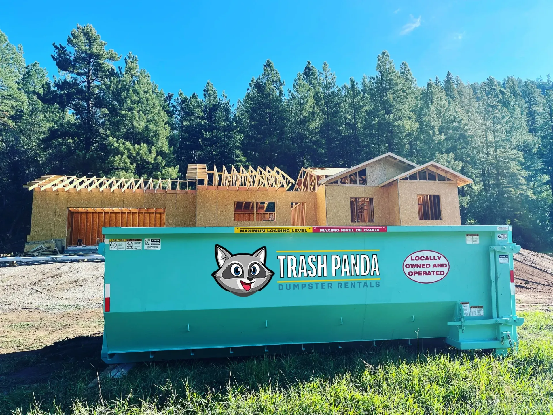 A green dumpster is parked in front of a house under construction.