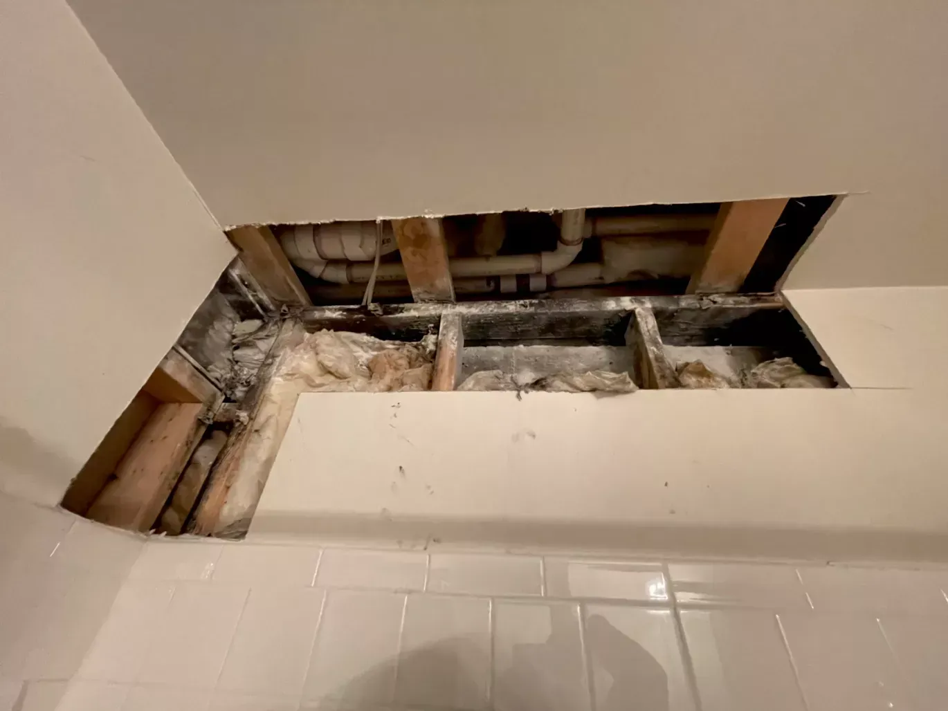 A hole in the ceiling of a bathroom with pipes coming out of it.