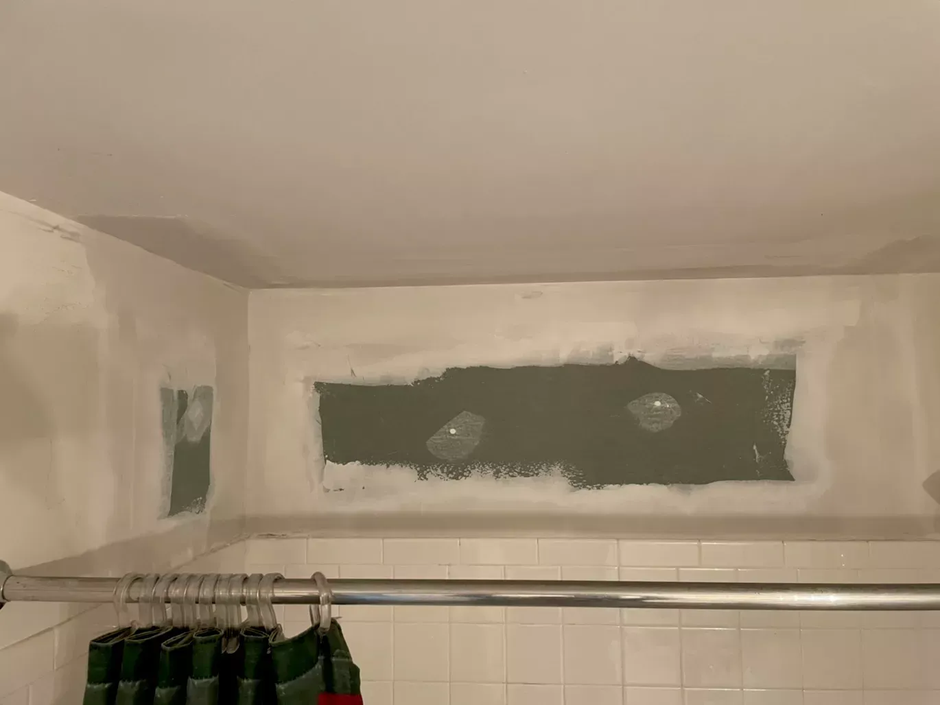 A bathroom with a shower curtain and a hole in the wall.