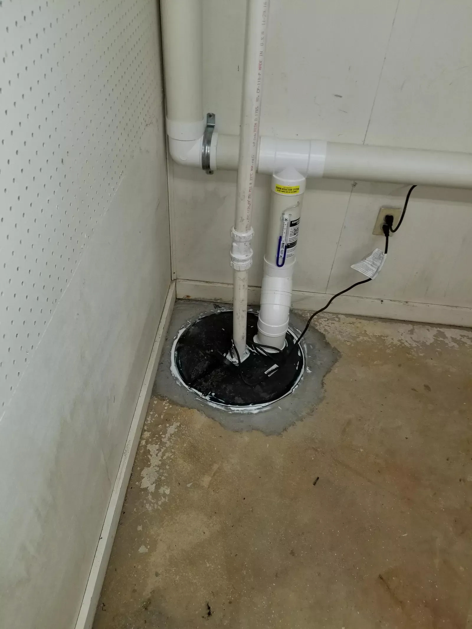 A basement pump is sitting in the corner of a room next to a wall.