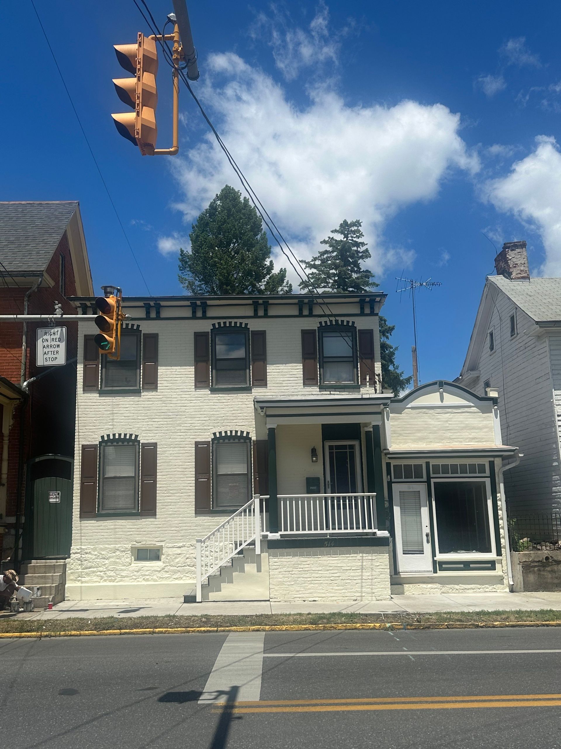A white house with brown shutters sits on the corner of a street