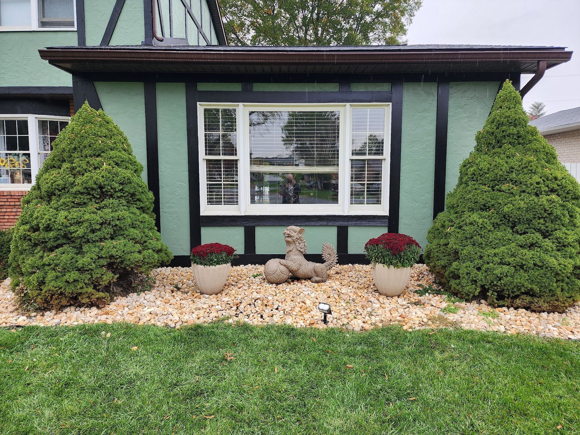 A green house with a large window and a garden in front of it.