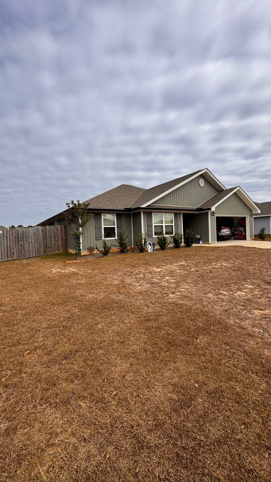 A grey, single-story suburban house with a two-car garage and a wooden privacy fence, set against a cloudy sky.
