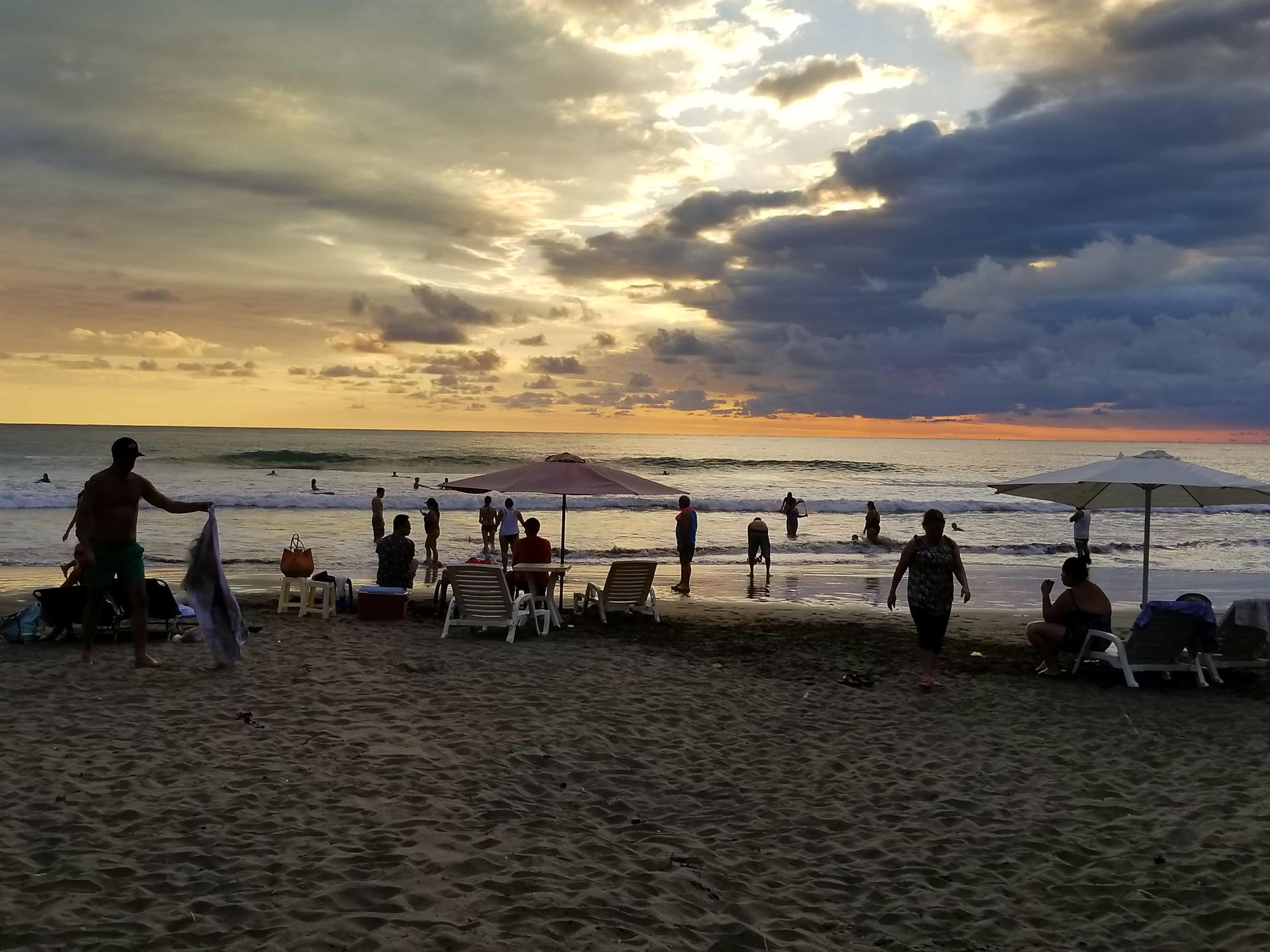 A group of people are standing on a beach at sunset.