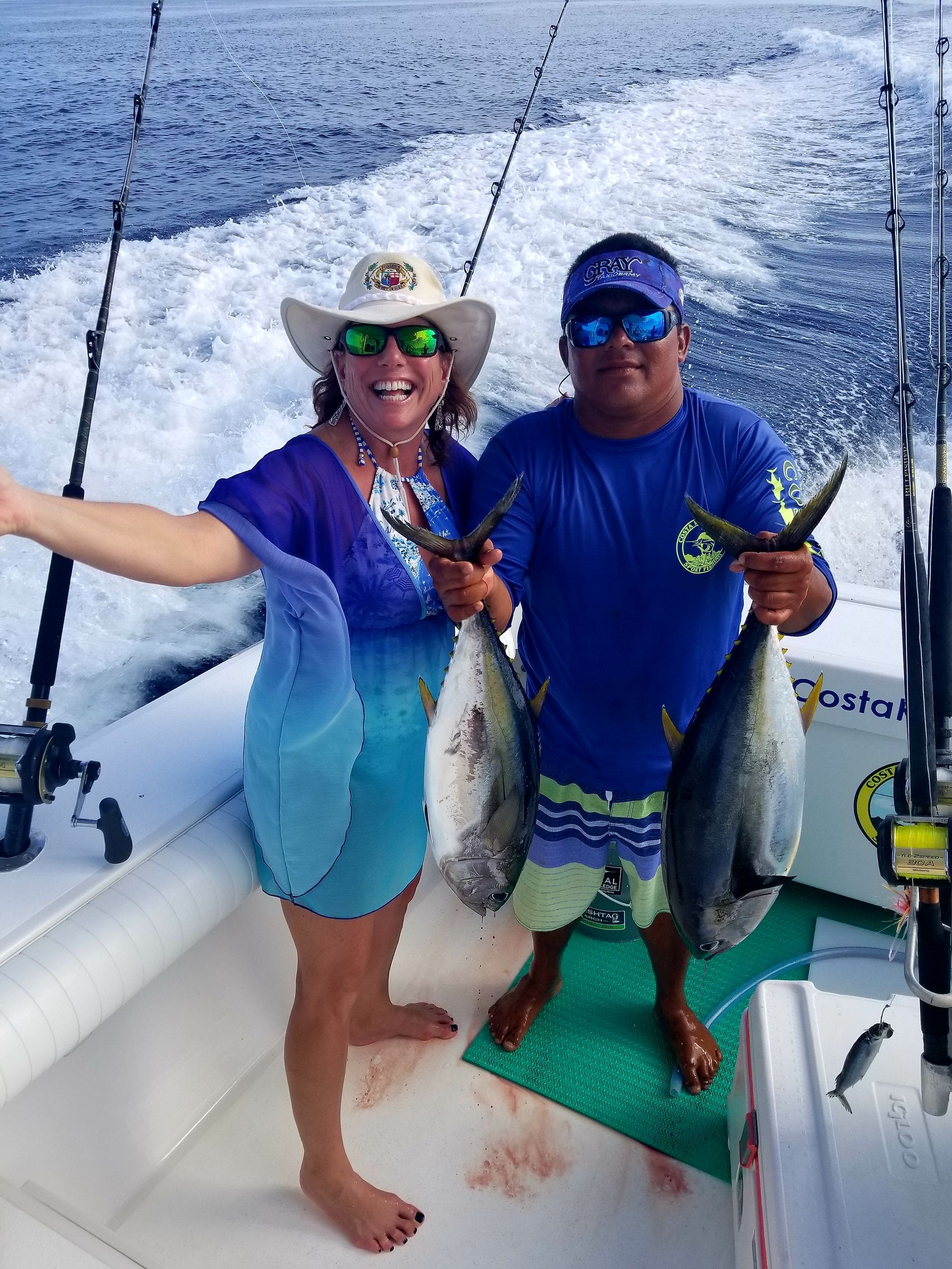 A man and a woman are standing on a boat holding fish.