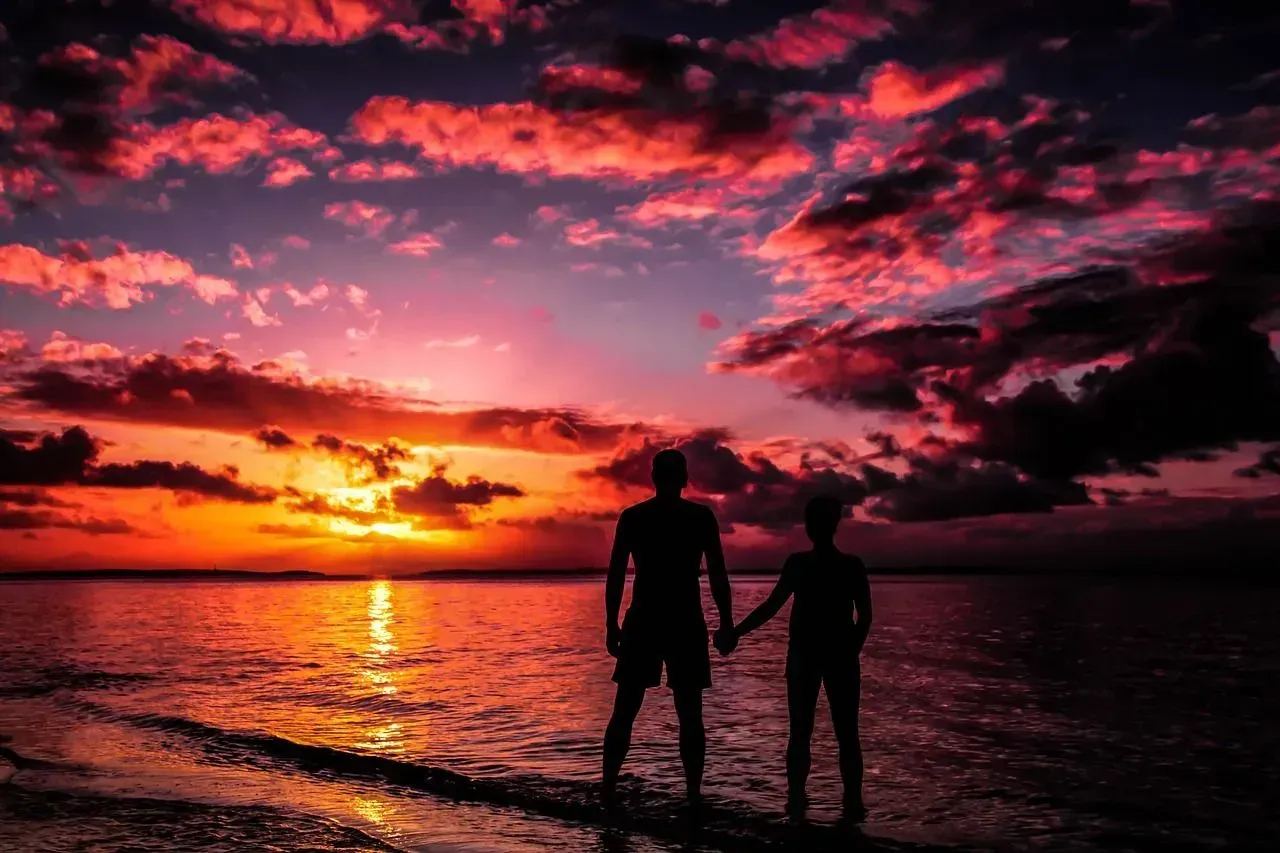 Two people are standing on a beach holding hands at sunset.