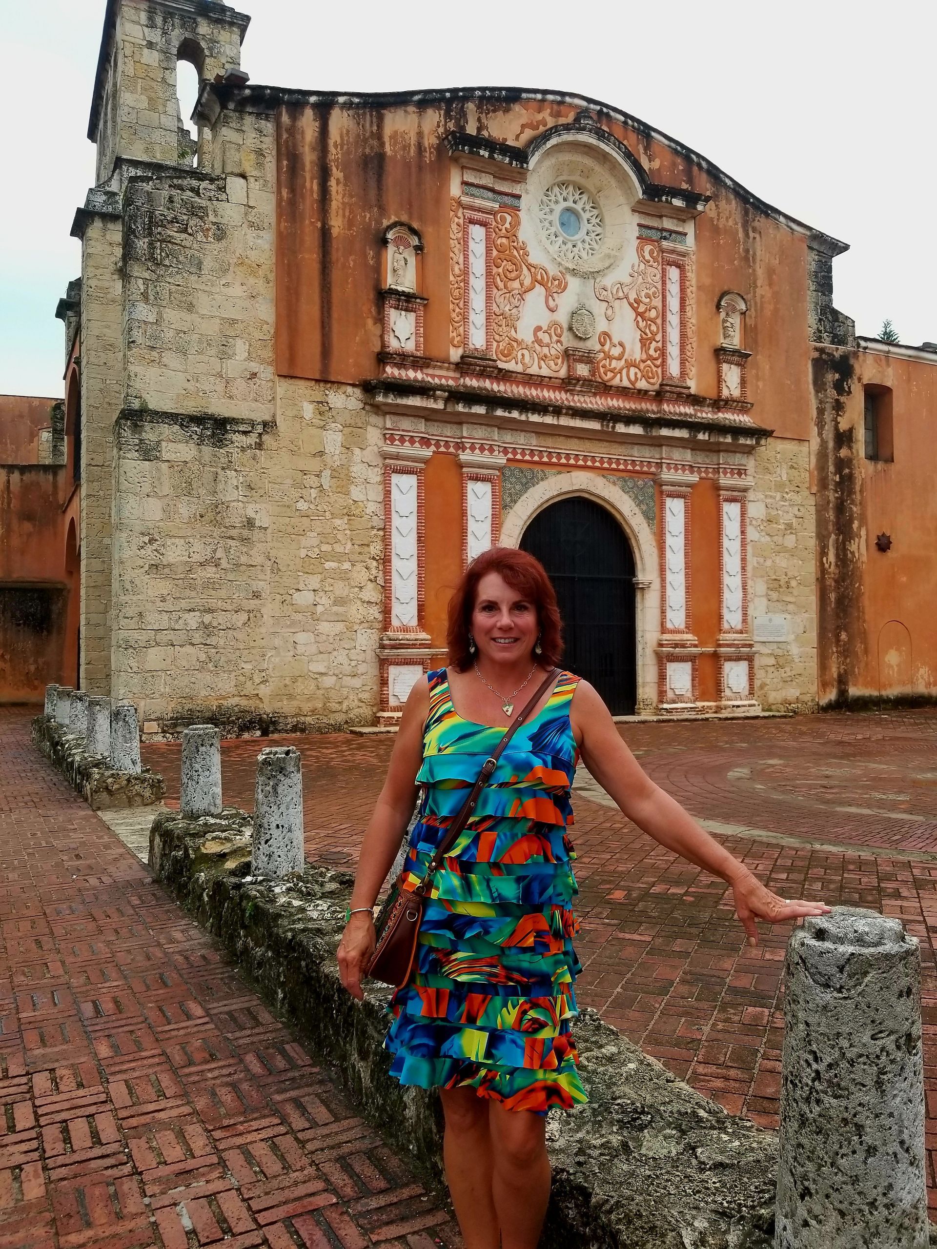 A woman in a colorful dress stands in front of an old building