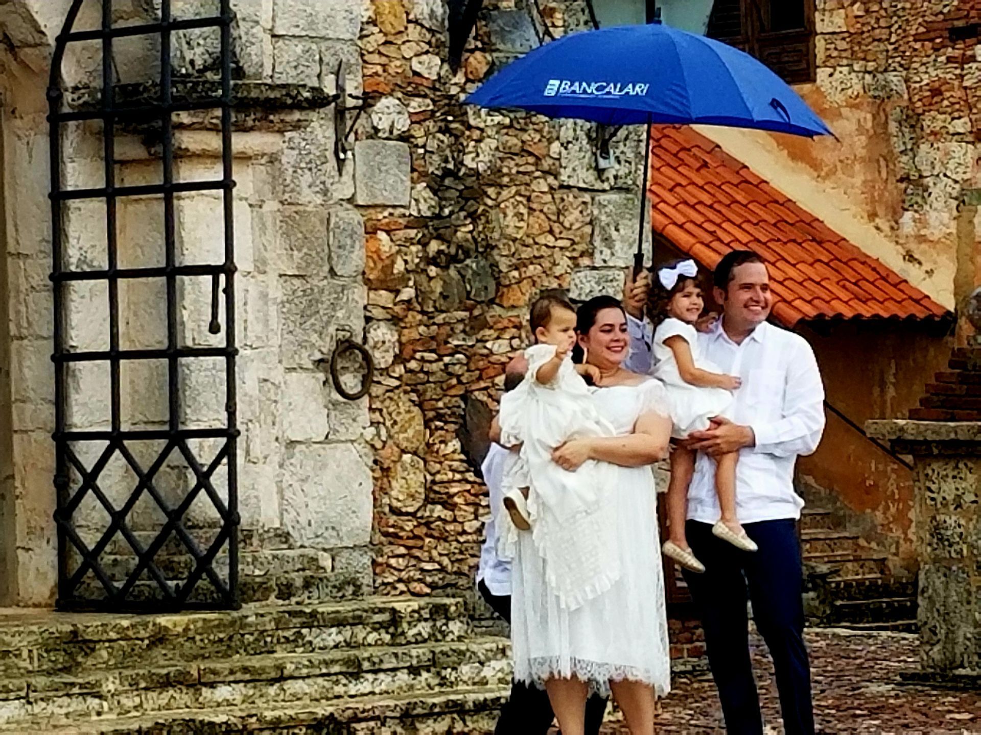 A family standing under a blue umbrella in front of a stone building