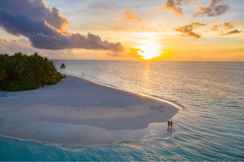 A couple is walking on a sandy beach at sunset.