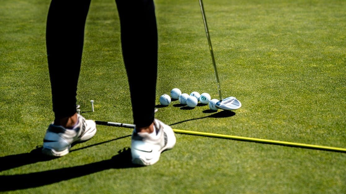 A person is standing on a golf course with golf balls and a golf club.