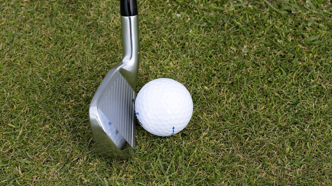 A golf club is hitting a golf ball on a green.