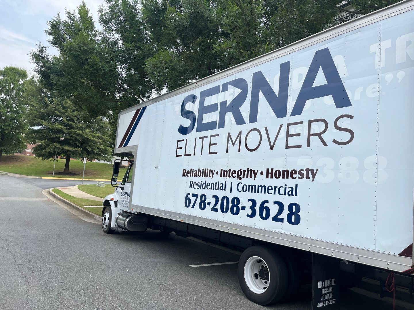 Serna Elite Movers truck parked on a residential street; blue and white lettering; phone number visible.