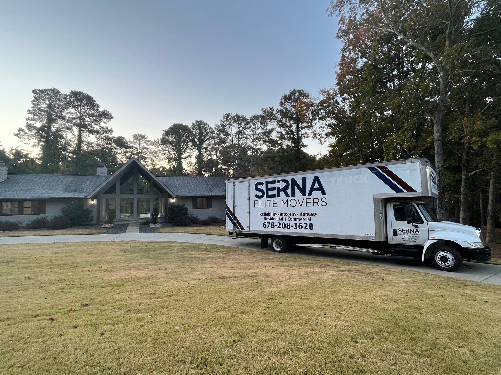 Moving truck parked in front of a house on a grassy lawn. The truck has 