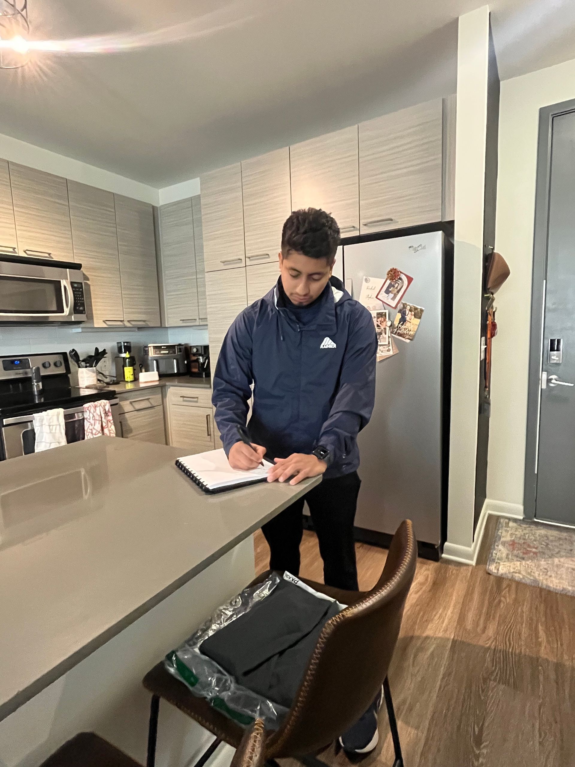 A man is sitting at a counter in a kitchen writing on a piece of paper.